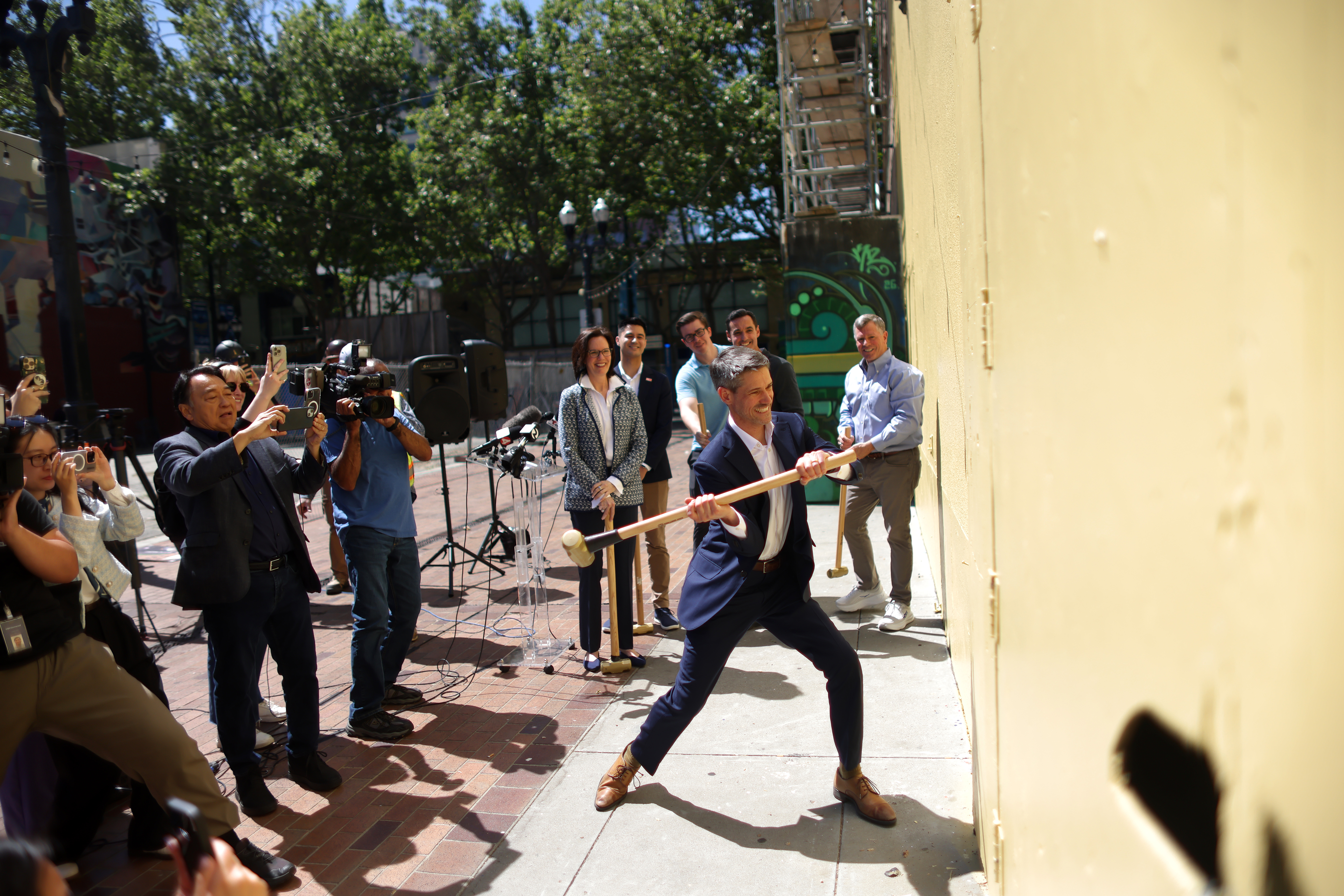 Mayor Matt Mahan uses a sledge hammer to knock a...