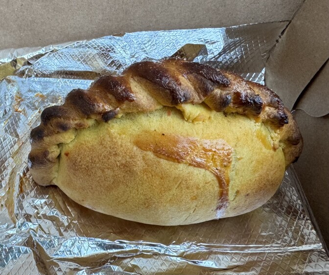 A beautiful brown empanada with a pinched top sits on a piece of silver foil.