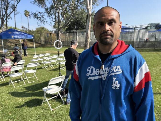 Male presenting person with a bald head. He is wearing a red, white, and blue sweatshirt that says "Dodgers."