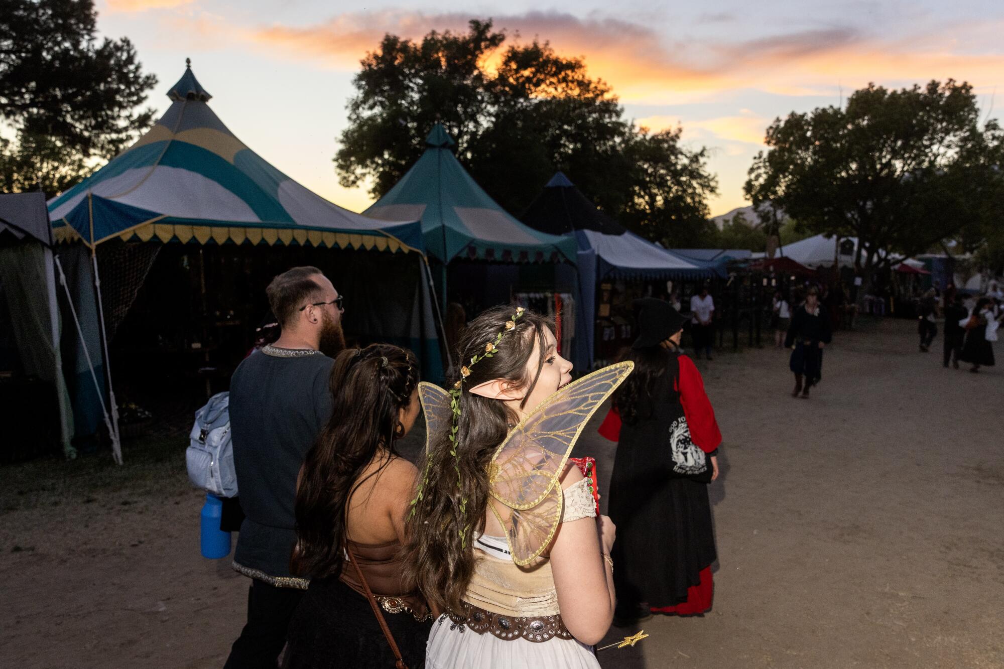A person dressed as a fairy walks with a ground past colorful tents