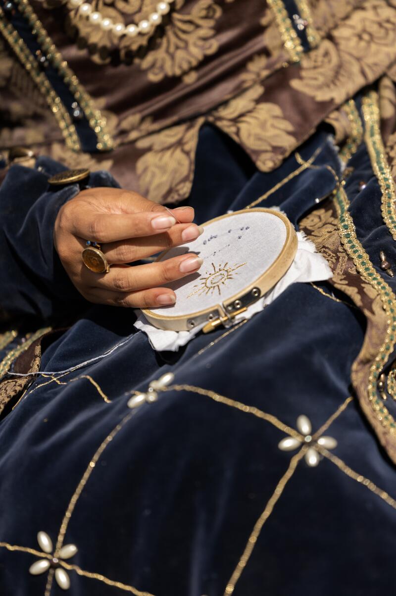 A maid of honor to the queen passes the time with canvas work.