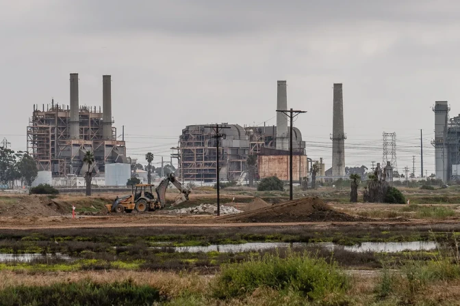 An oil and production site with construction equipment and power poles nearby.