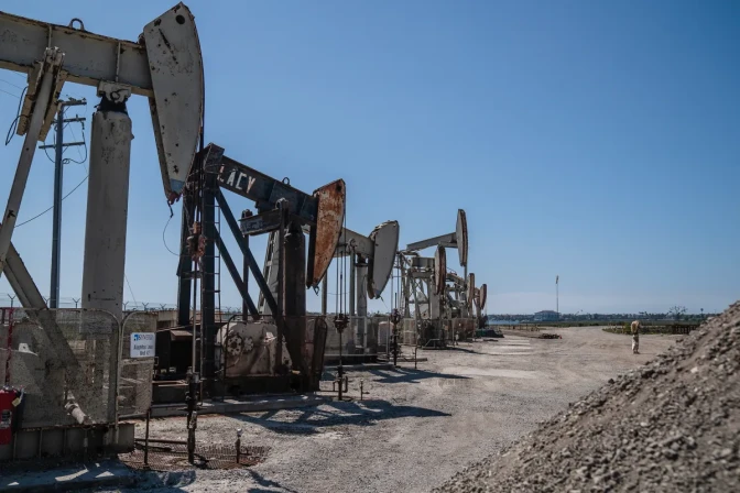 A row of oil wells near a pile of dirt.