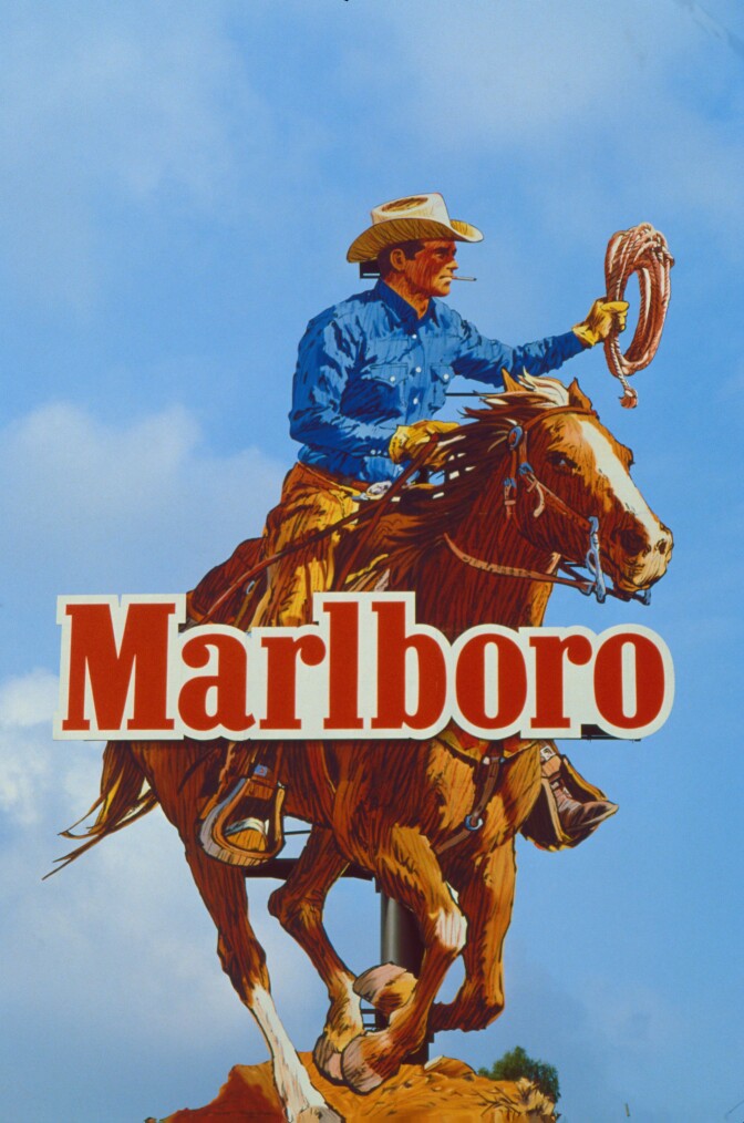 A giant billboard of a cowboy smoking a cigarette holding a lasso for Marlboro.