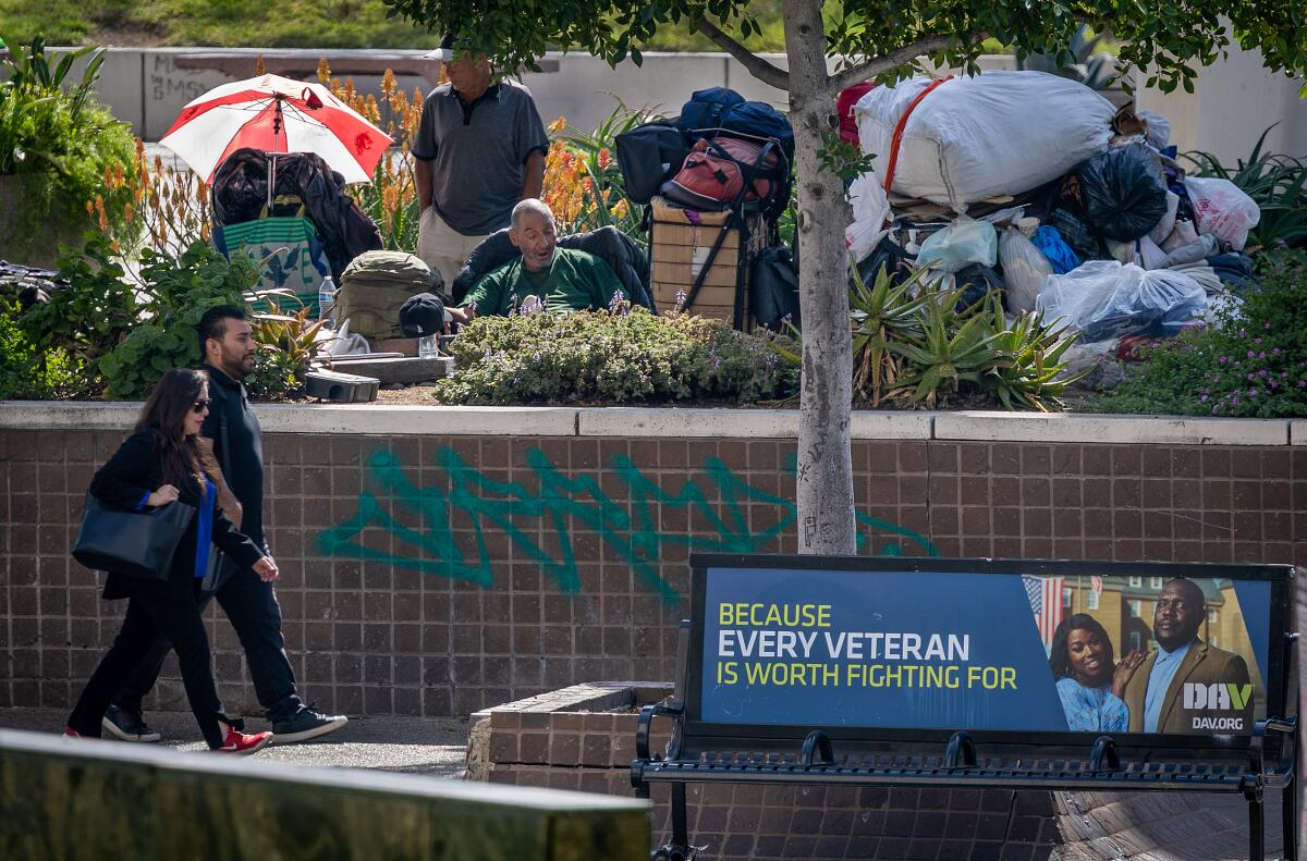 Homess people and their belongings sit amid landscaping at Fletcher Brown Square near the Los Angeles Mall.