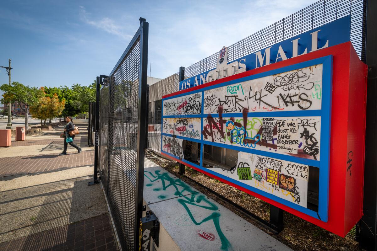 A person walks by a broken and graffiti-marked Los Angeles Mall sign, across the street from Los Angeles City Hall.