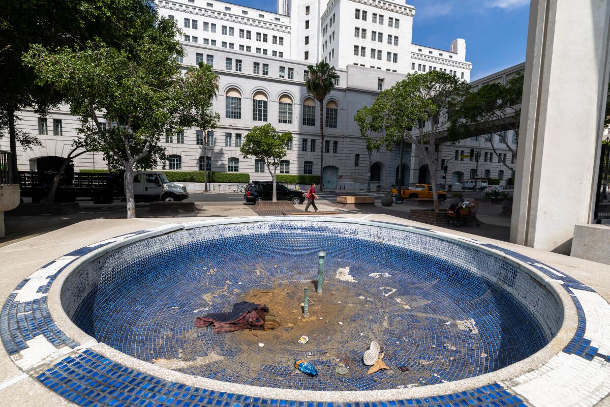 A person walks by trash in a broken and empty fountain at Felipe de Neve Plaza, next to Los Angeles City Hall East.
