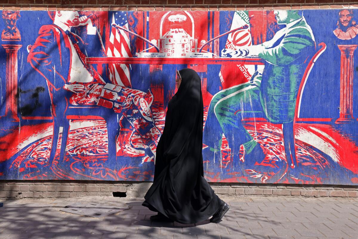 A woman walks past an anti-U.S. mural depicting Iran-U.S. talks near the former U.S. embassy