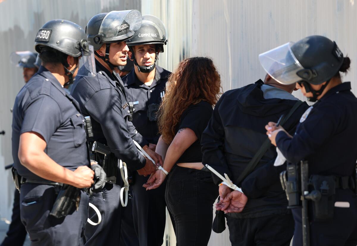 LAPD officers take a demonstrator into custody following a protest against ICE at the Metropolitan Detention Center.