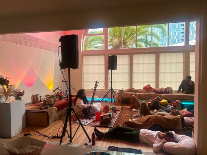 A group of people lie on the ground while a musician plays on a sitar.