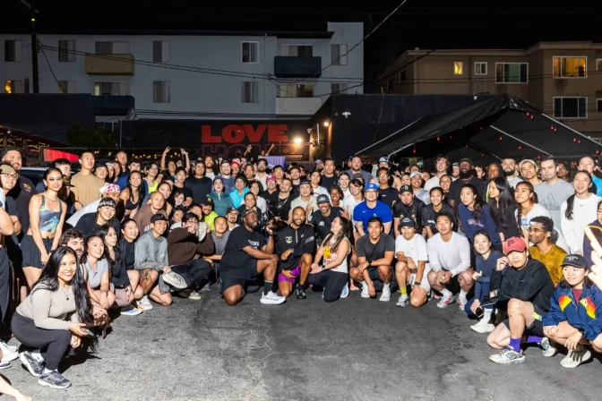 A crowd of people in running gear pose for a photo outside next to a canopy and mural painted Love Hour. There are apartment buildings in the background.