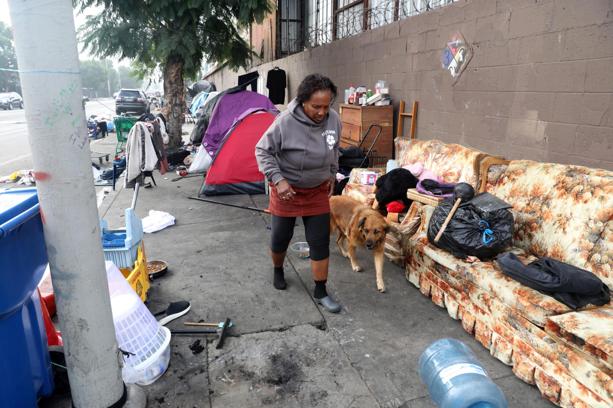 A homeless woman is shown with her dog at a homeless encampment along Avalon Boulevard.