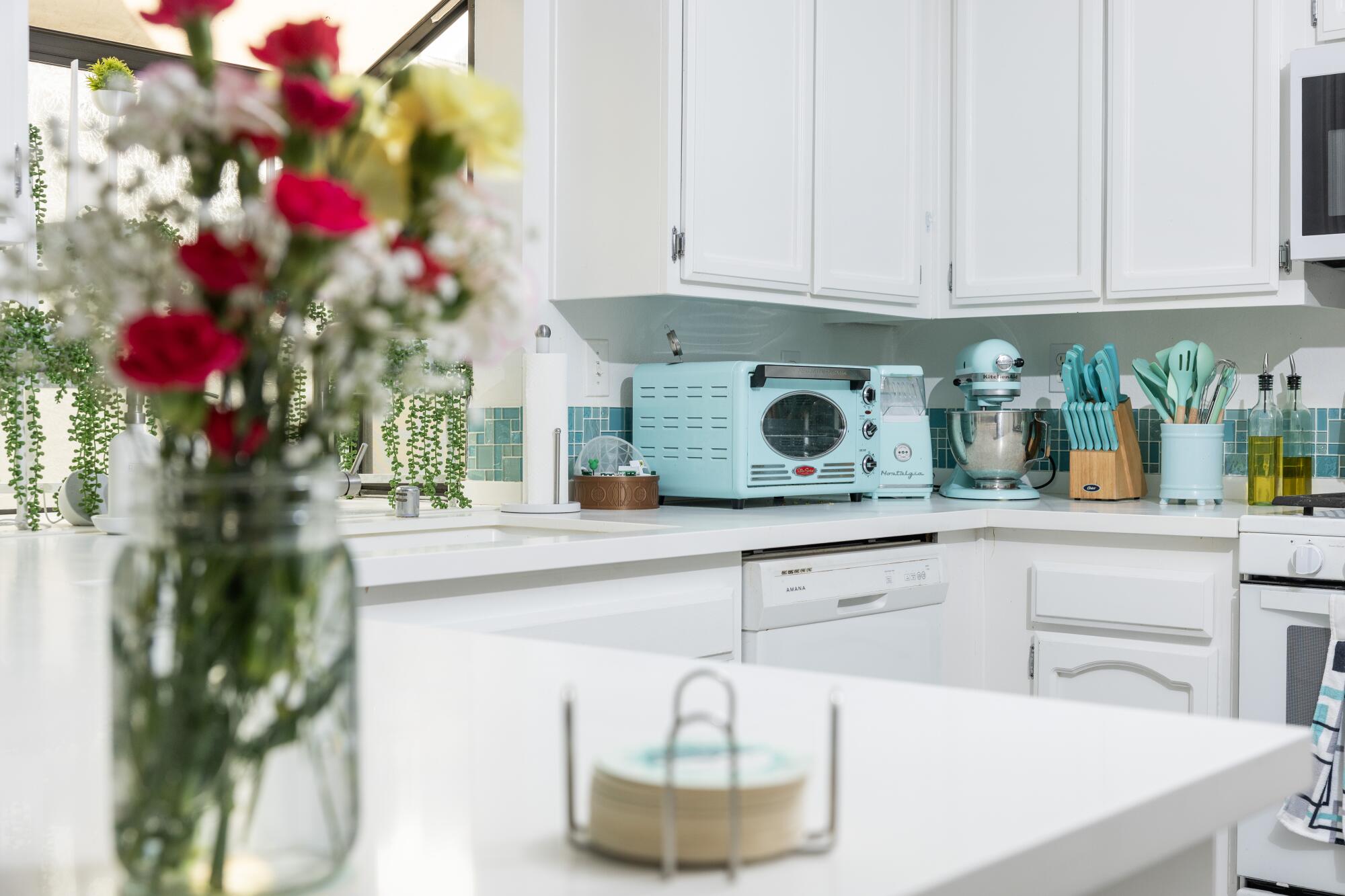 A blue and white kitchen with flowers and appliances and accessories on the countertop.
