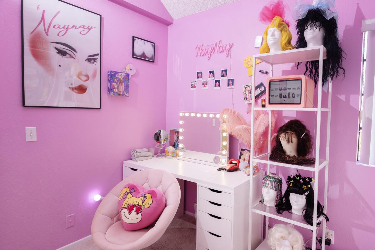 A pink and white room with wigs and a makeup dresser 