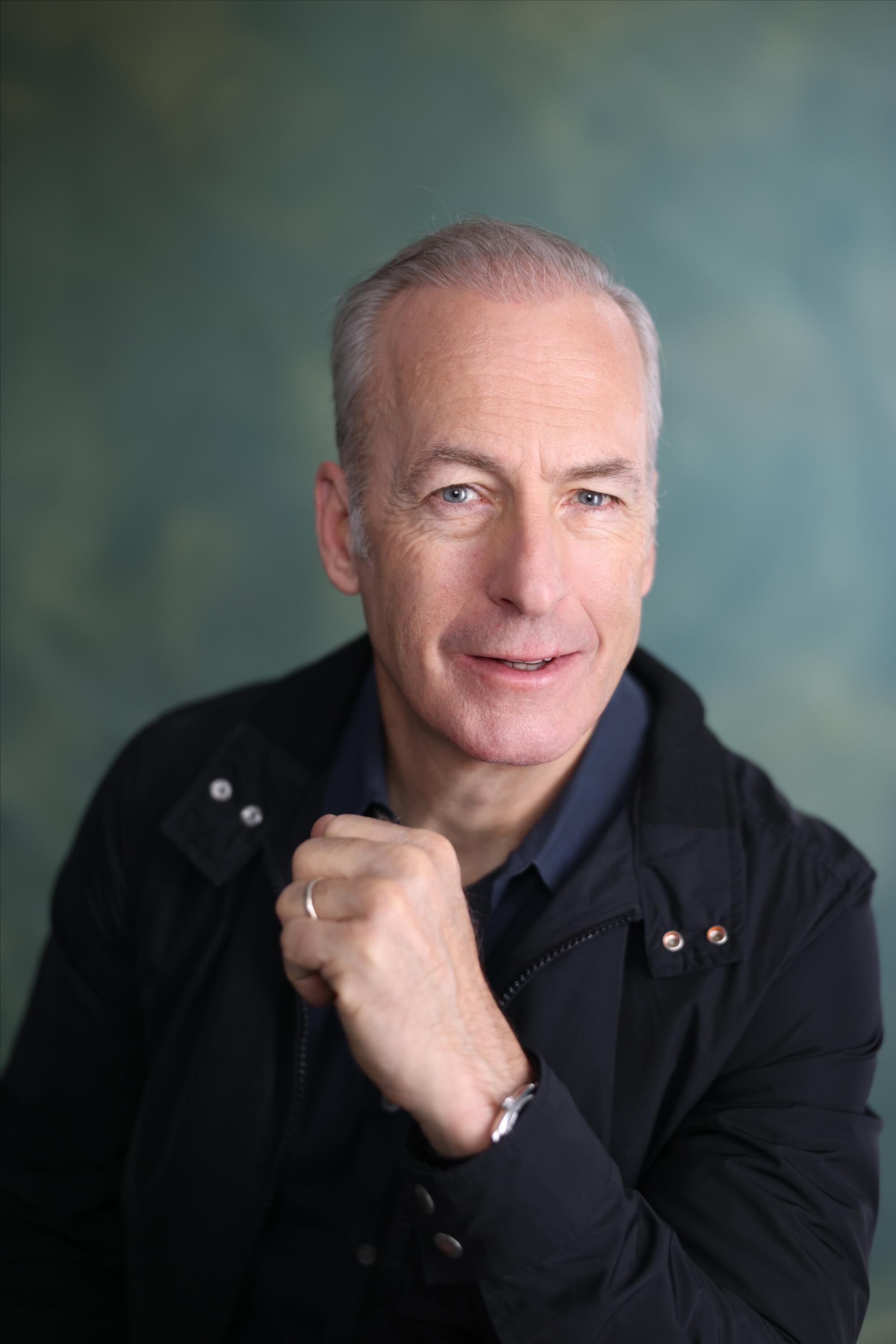 A man in a dark top smiles at the lens.