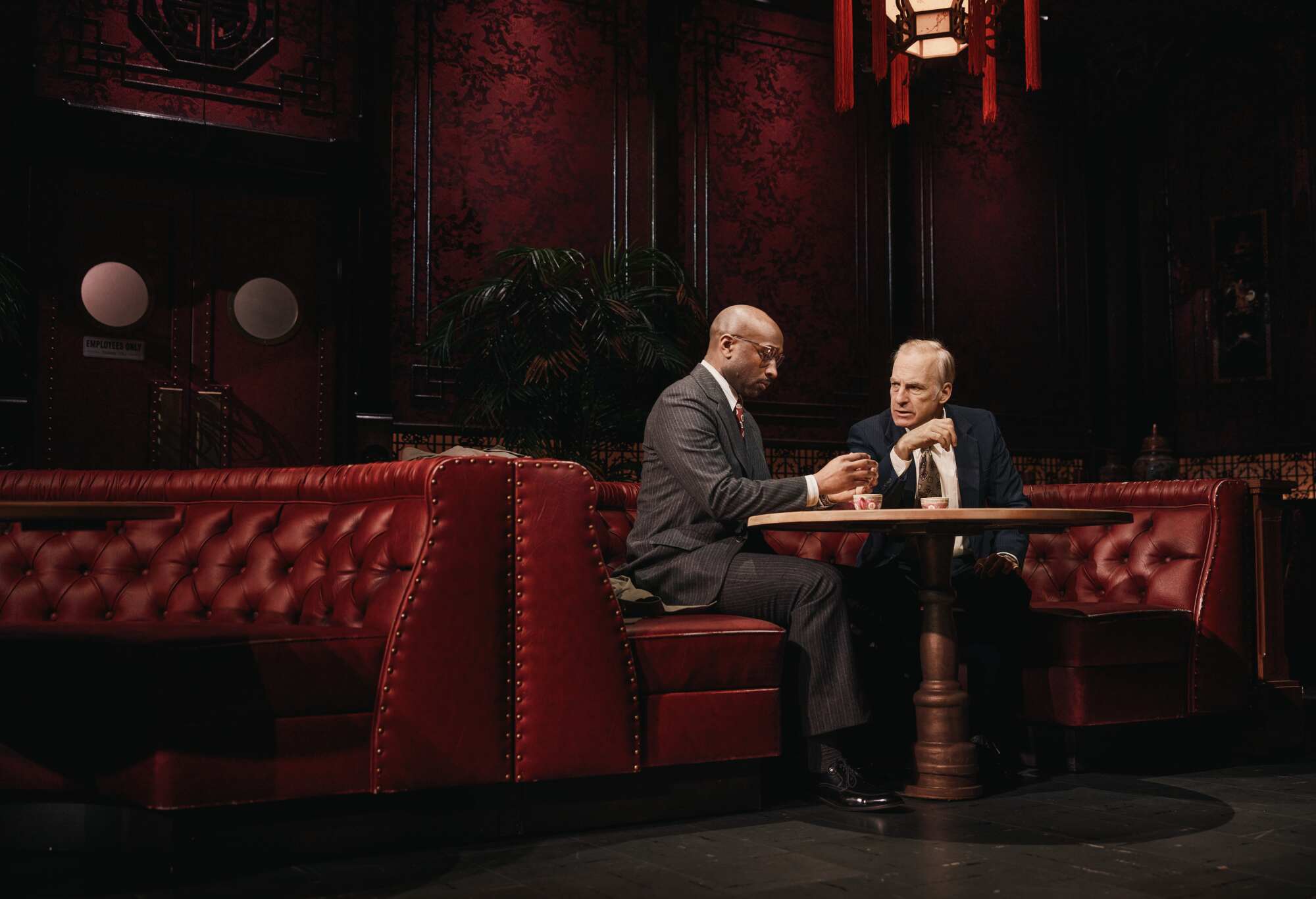 Two salesmen in suits sit in a bar booth discussing leads.