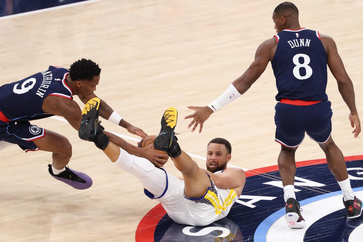 Stephen Curry falls to the court to grab a loose ball against Clippers Bennedict Mathurin and Kris Dunn in the third quarter.