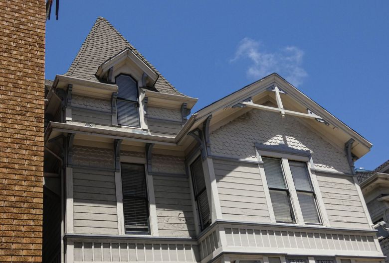 A view of the upper floors of a 19th century white Victorian home, with a peaked "witch's hat" roof