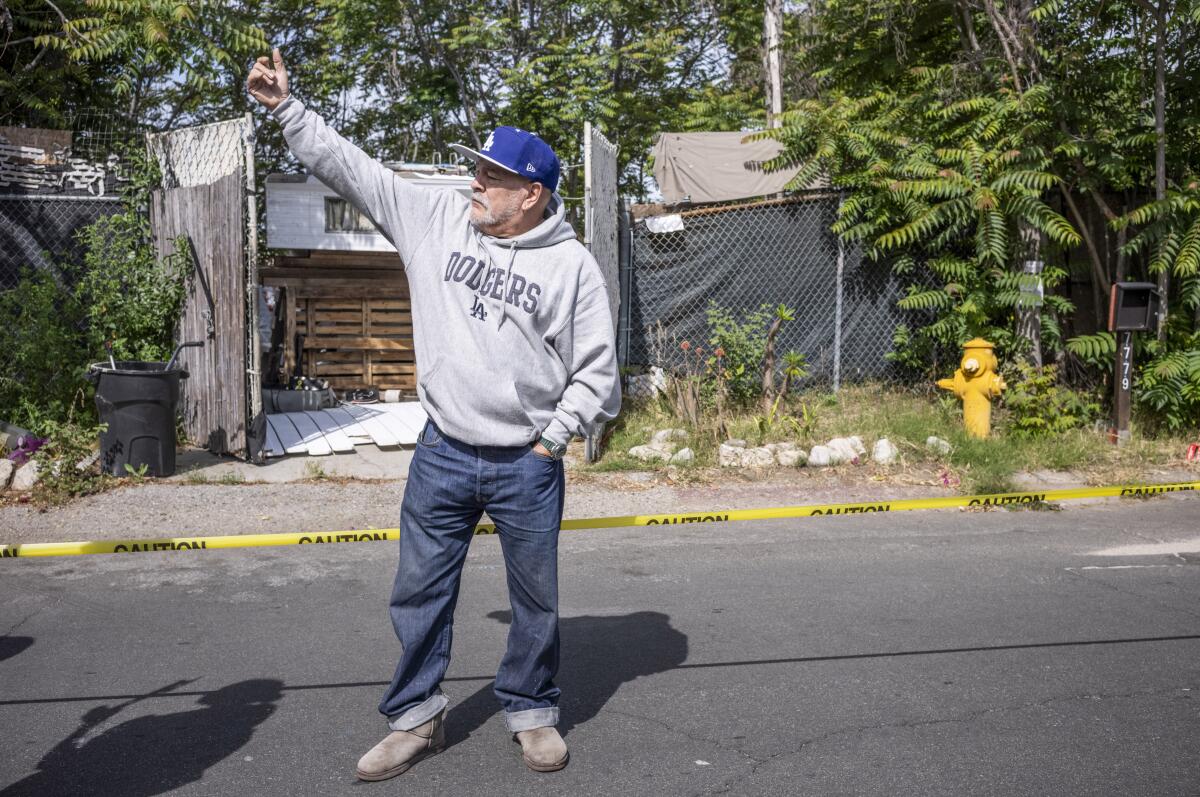 A man waves to a neighbor as workers remove debris from a homeless encampment near his home.