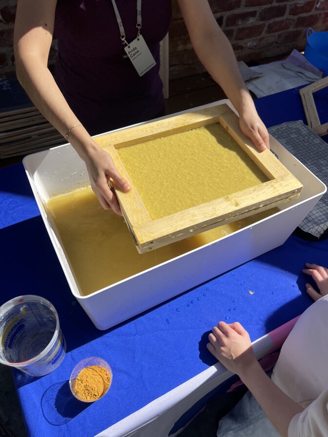 Two hands hold a wooden frame filled with paper pulp.