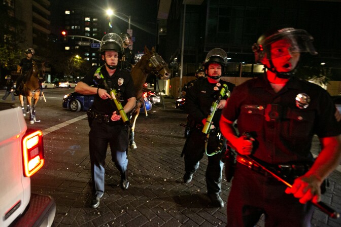 LAPD officers in uniform with riot gear move in the street.