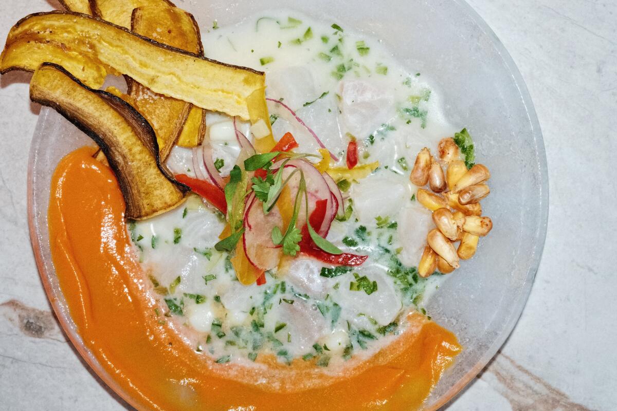 A bowl of white fish ceviche with sweet potato, cancha, plantain chips and coconut leche de tigre on a white marble table