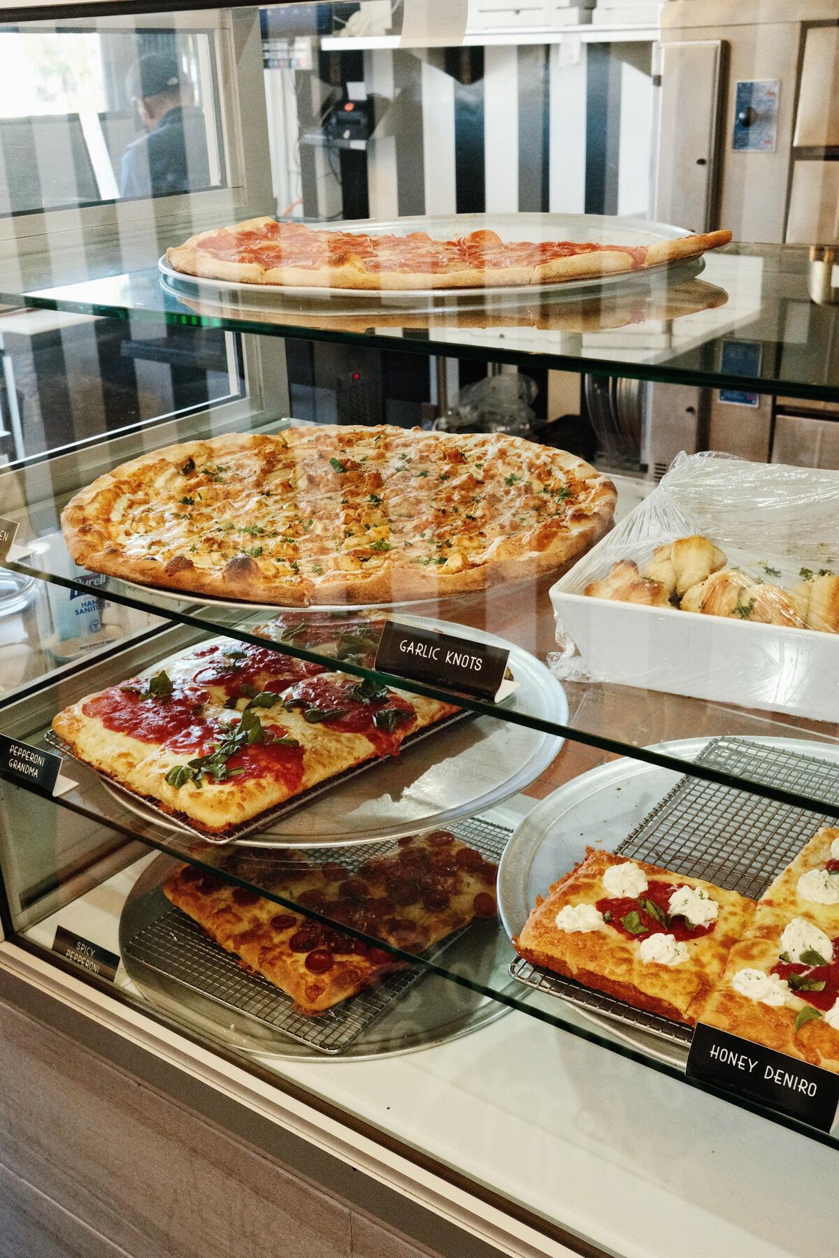 By-the-slice New York-style pizzas and square pies in the glass case at Brooklyn Square Downey