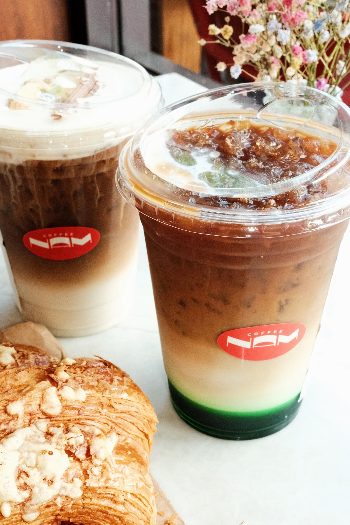 A pandan iced latte, right, with a banana iced latte and croissant at Vietnamese coffee shop Nam Coffee