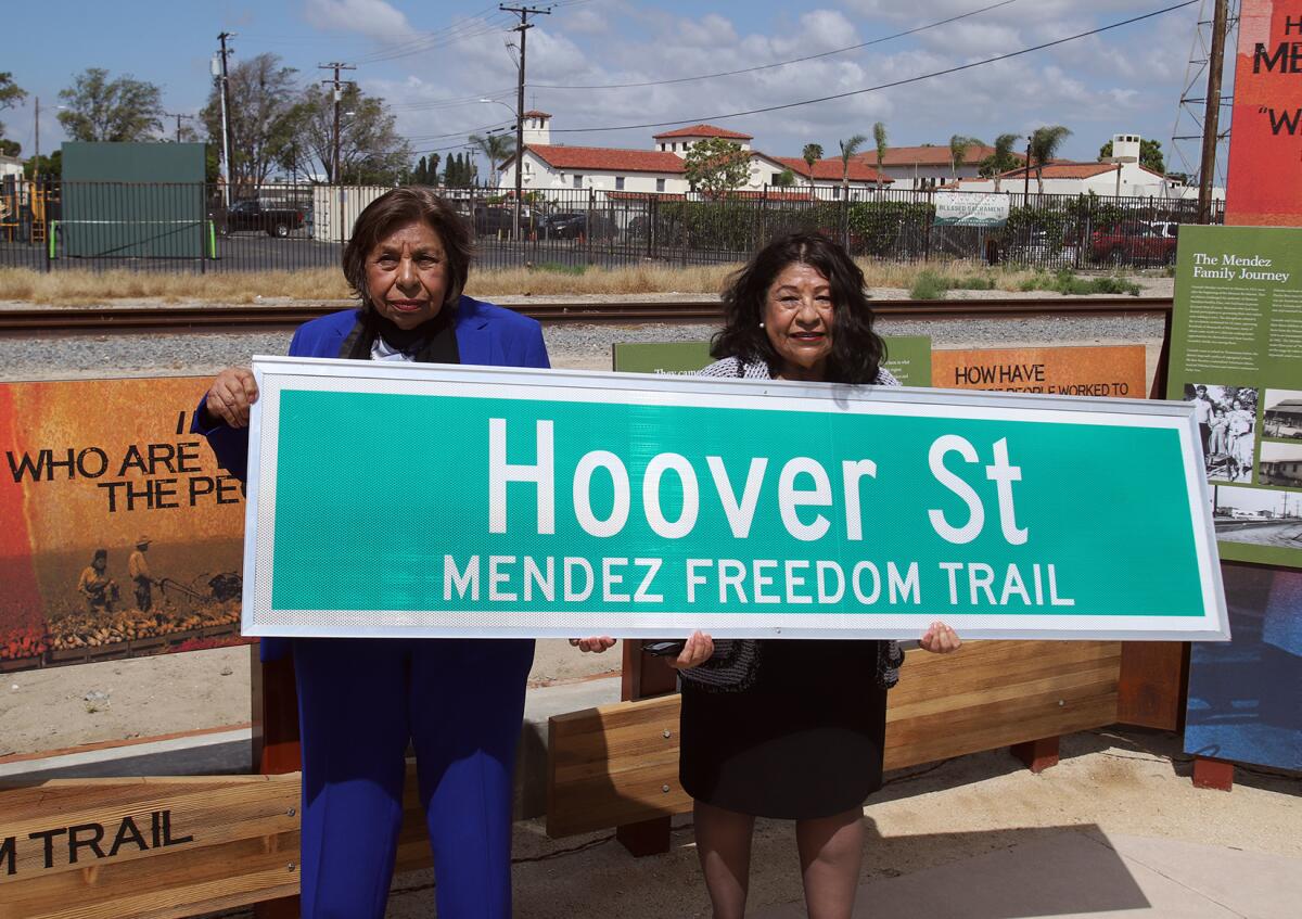 Sylvia Mendez, left, and sister Sandra Mendez Duran hold the new Hoover Street Mendez Freedom Trail street sign.