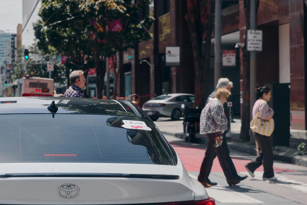 Pedestrians cross the street in front of a Lyft and Uber driver.