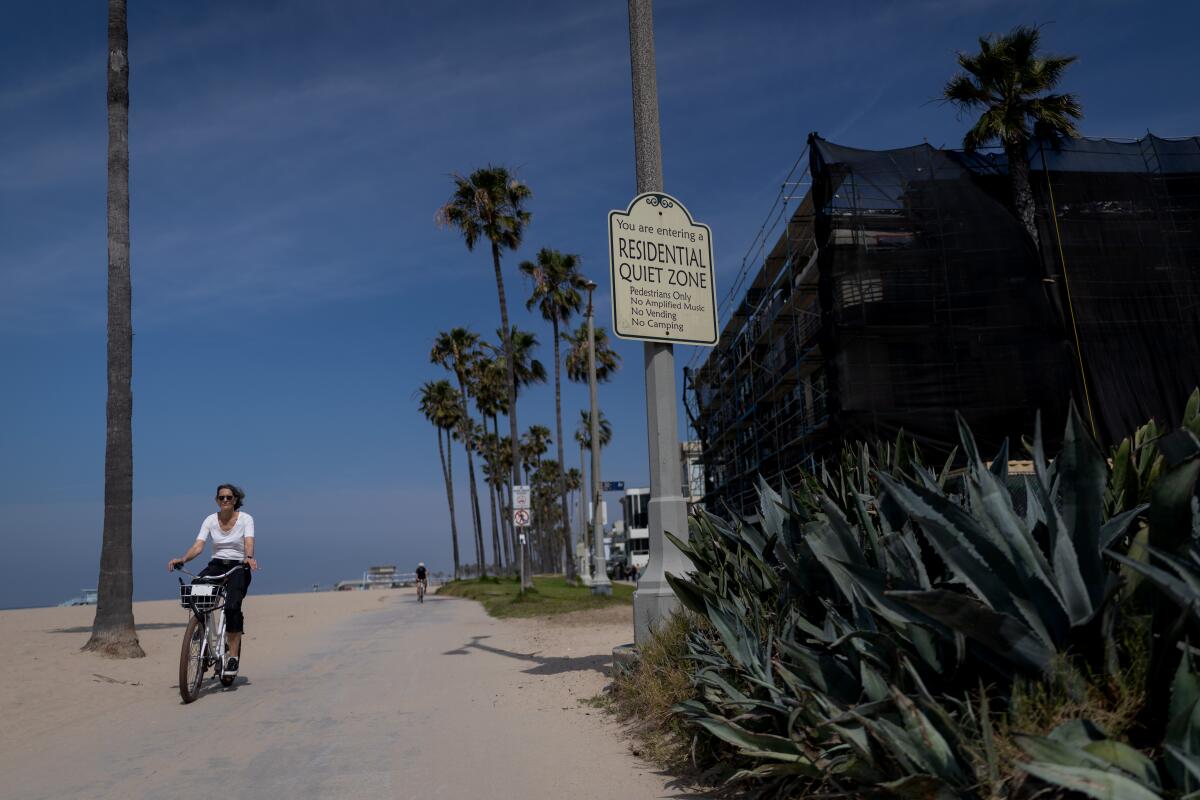 A woman rides along the boardwalk in Venice past signage indicating a quiet zone.
