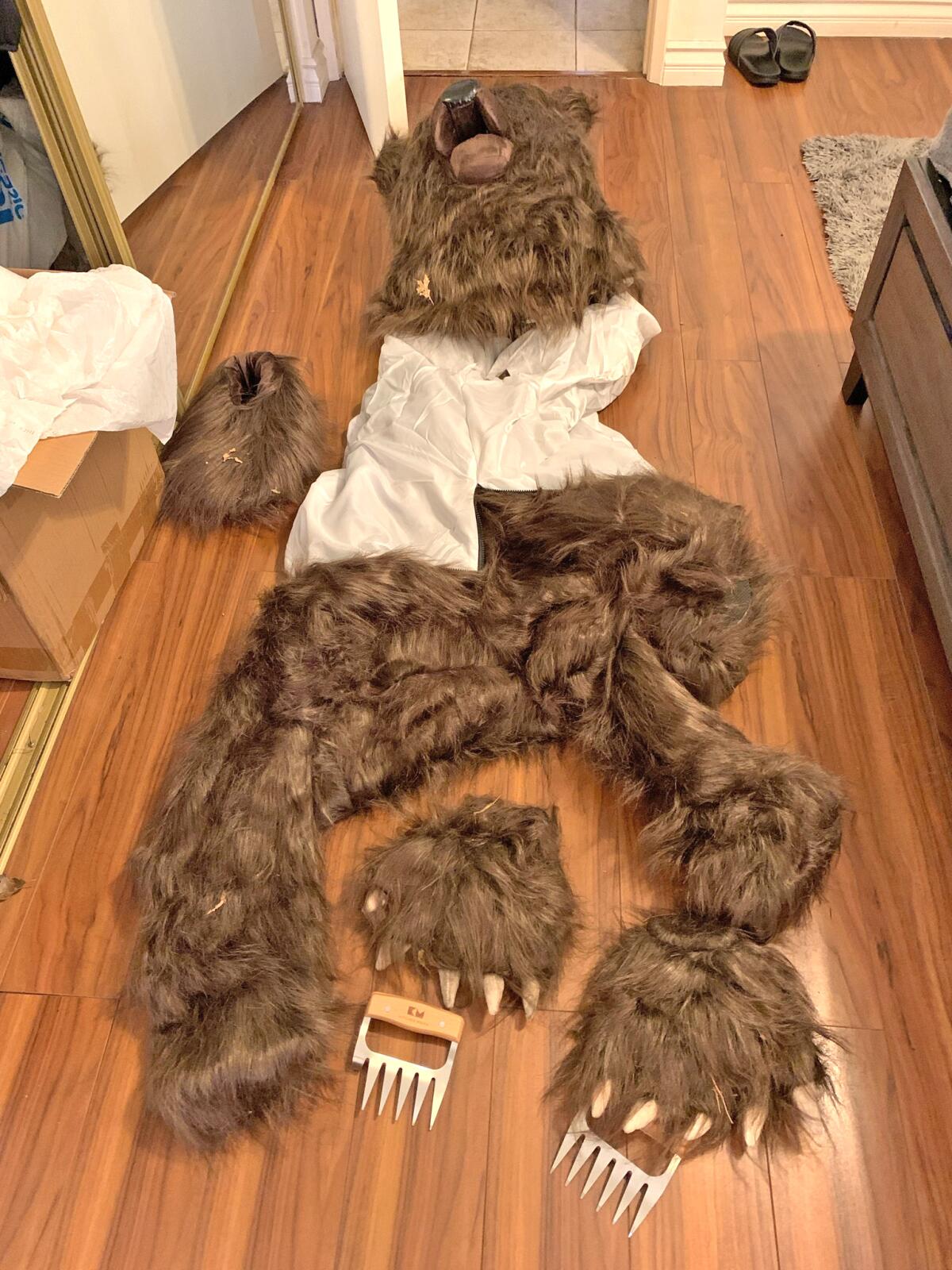 A bear suit, complete with claws, lying on a floor