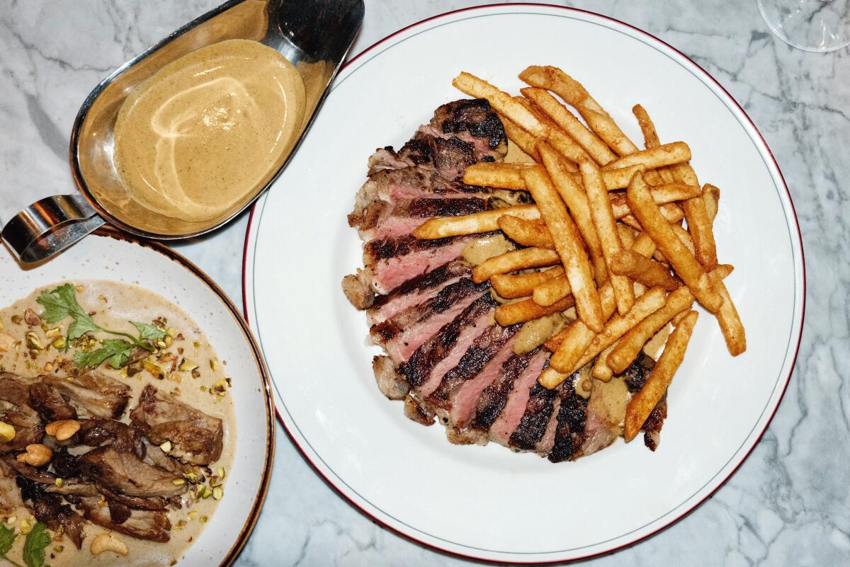 A plate of steak frites served with masala au poivre along with a bowl of lamb neck korma on a white marble table