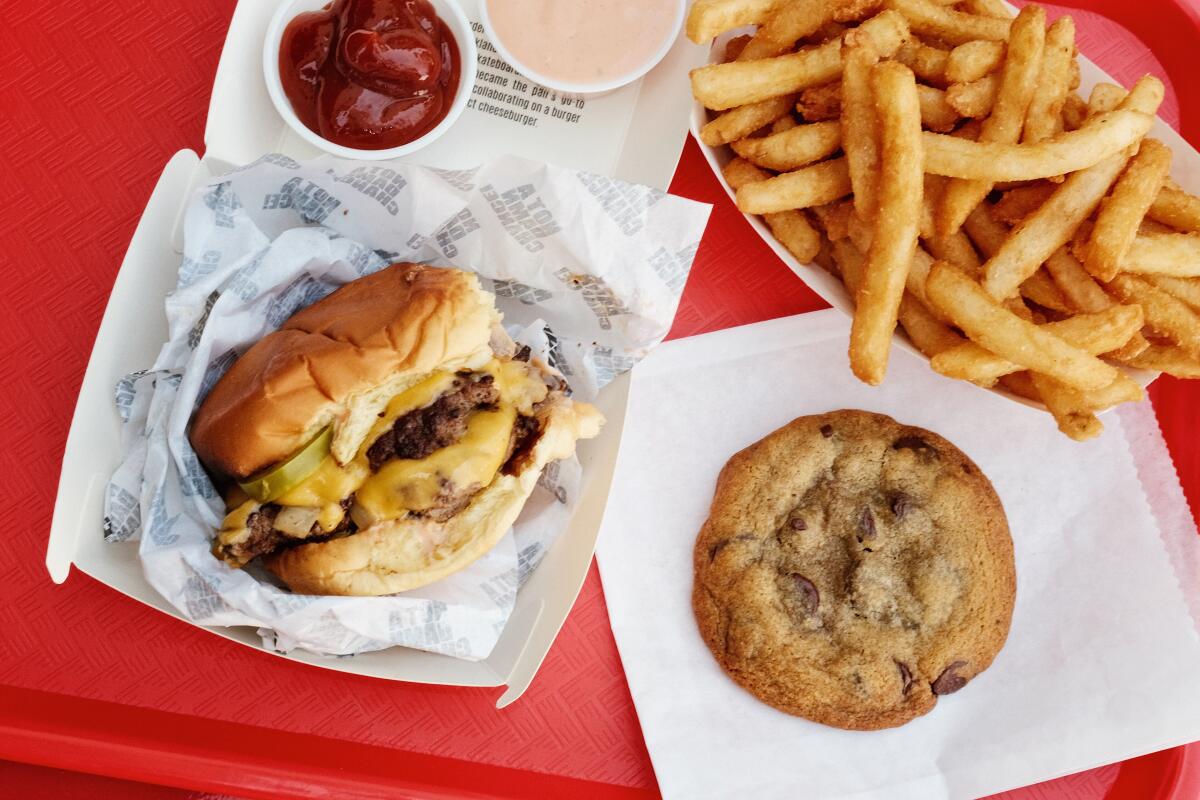 A double cheeseburger, cookie, fries and dipping sauces on a bright red plastic tray