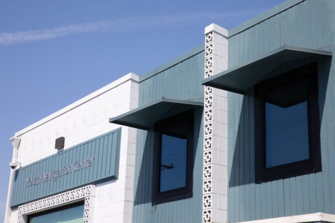 A slightly low angle view of a building with white and blue walls, three windows, and signage that reads "Youth Navigation Center."