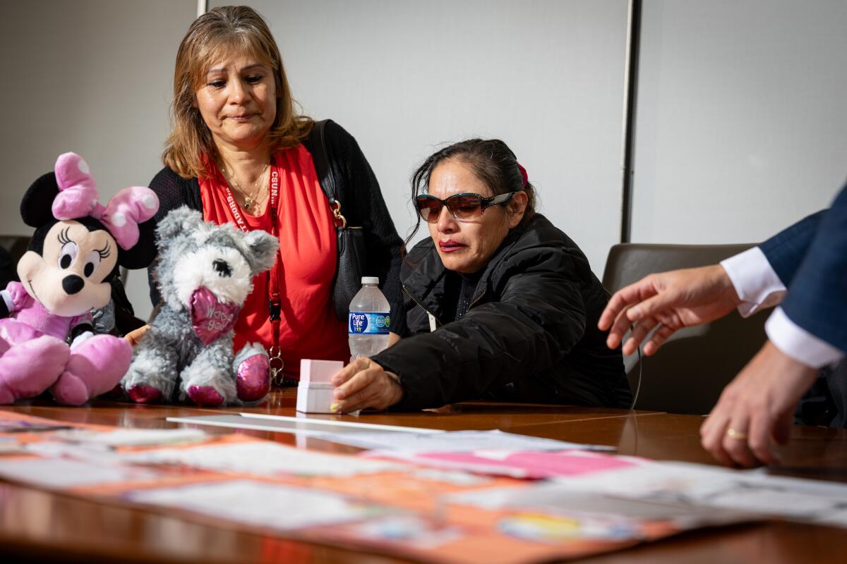 Two women sit with a pair of stuffed animals at a conference table.