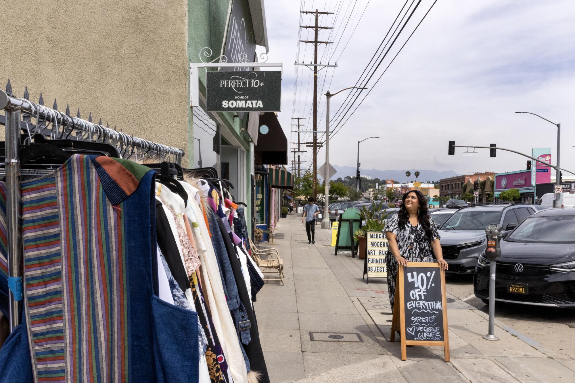 Marcy Guevara-Prete holding onto a sign outside her store that reads, "Entire Store 40% off, Size 10+."