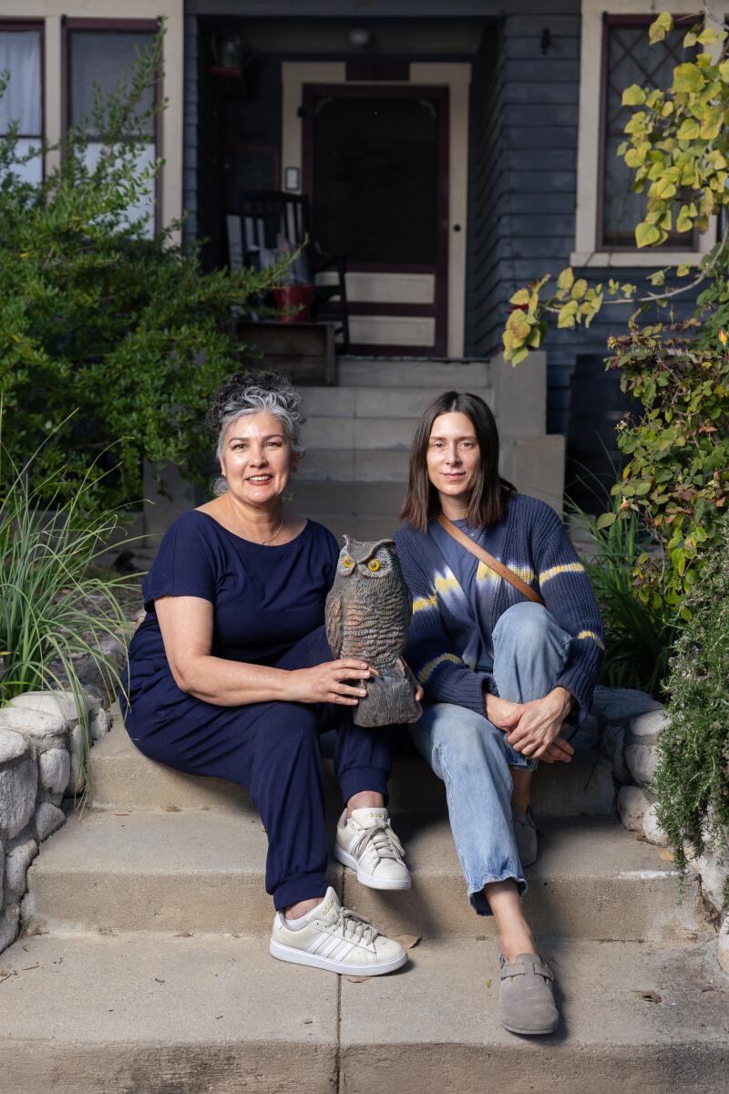 Two women sit on steps with a fake owl.