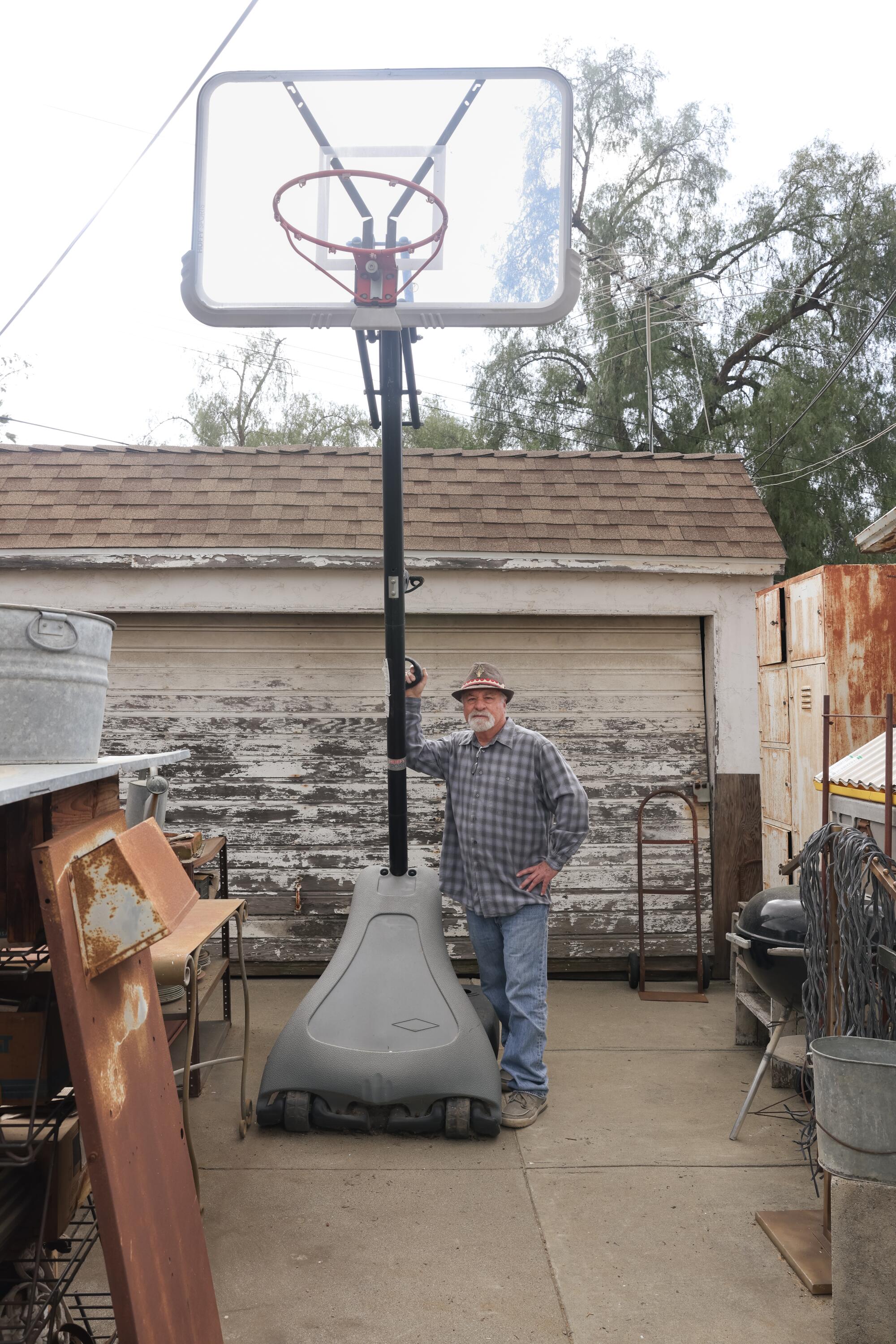 A man poses next to a basketball hoop in front of his garage.