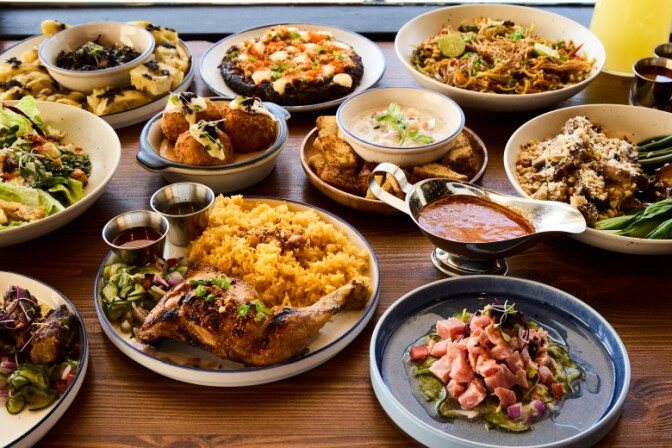 A top-down view of a wooden table covered in various Filipino dishes. Featured items include grilled chicken with yellow rice and more.