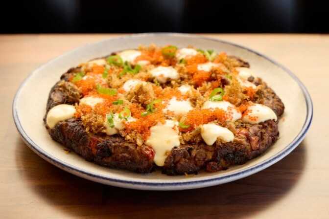 A close-up of a circular Filipino eggplant omelet on a white plate. The dish is topped with creamy white sauce, orange fish roe (tobiko), shredded crab meat, and sliced green scallions.
