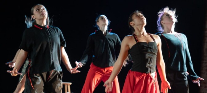 Four women of various skin tones dance, holding their arms by their sides while they look upward. 