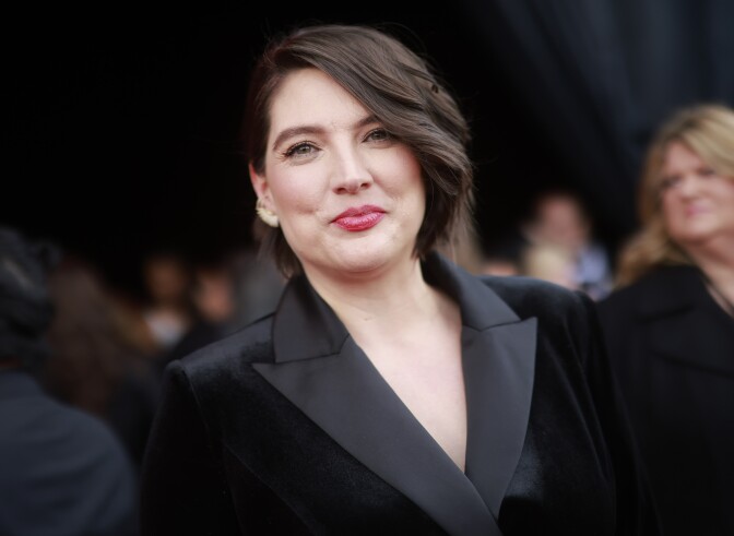 A light-skinned woman wearing a black suit looks at the camera. 