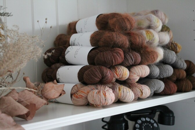 Several bolts of yarn in various shades of brown, pink and gray stacked on a shelf.