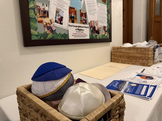 Different colored kippahs in a basket on a table covered with a white cloth. 