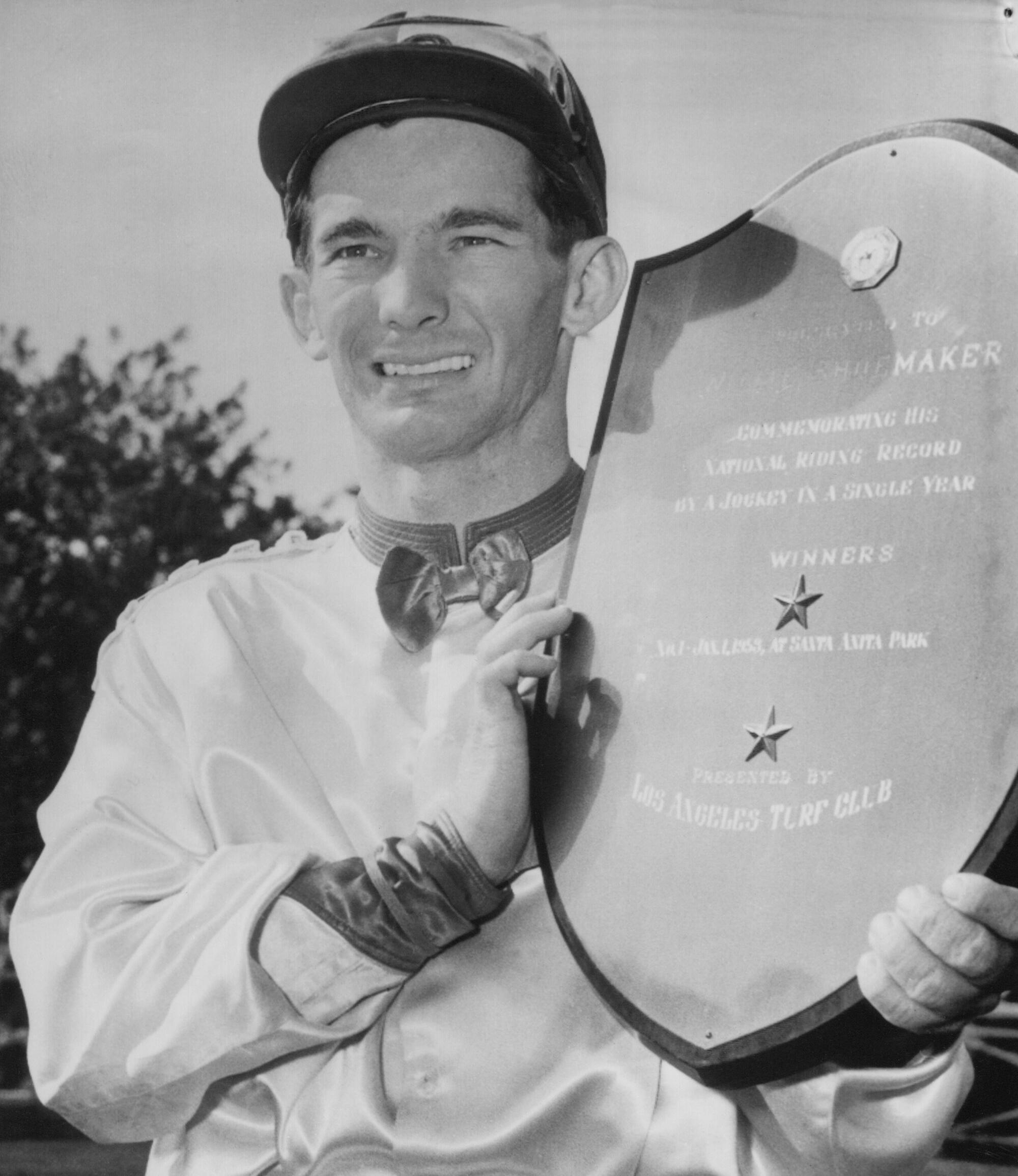 Jockey Bill Shoemaker smiles as he holds a large plaque presented to him at Santa Anita in 1953 for winning 484 races. 