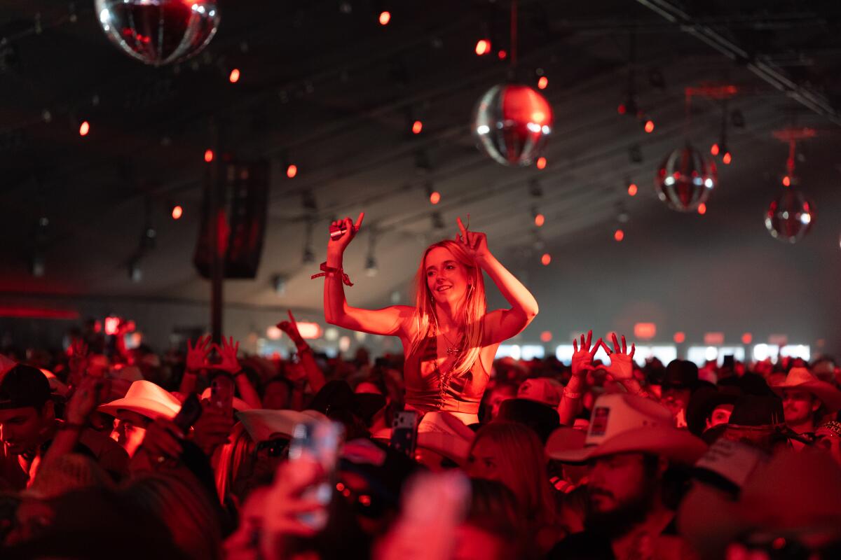 A woman on top of someone's shoulders dances under a disco ball inside a tent at Stagecoach 2026