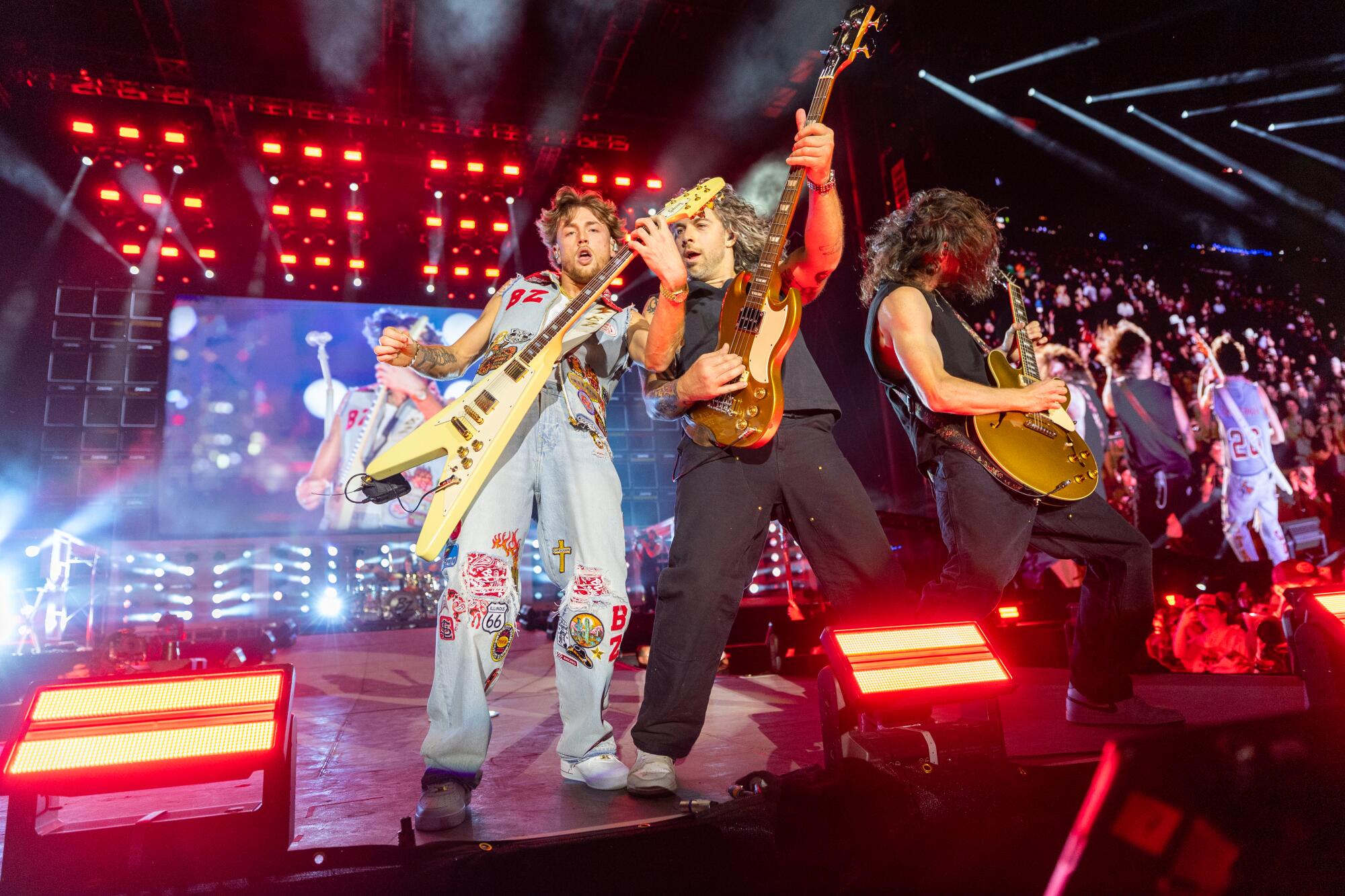 Bailey Zimmerman plays guitar with two other guitarists on a stage lit in red at Stagecoach 2026