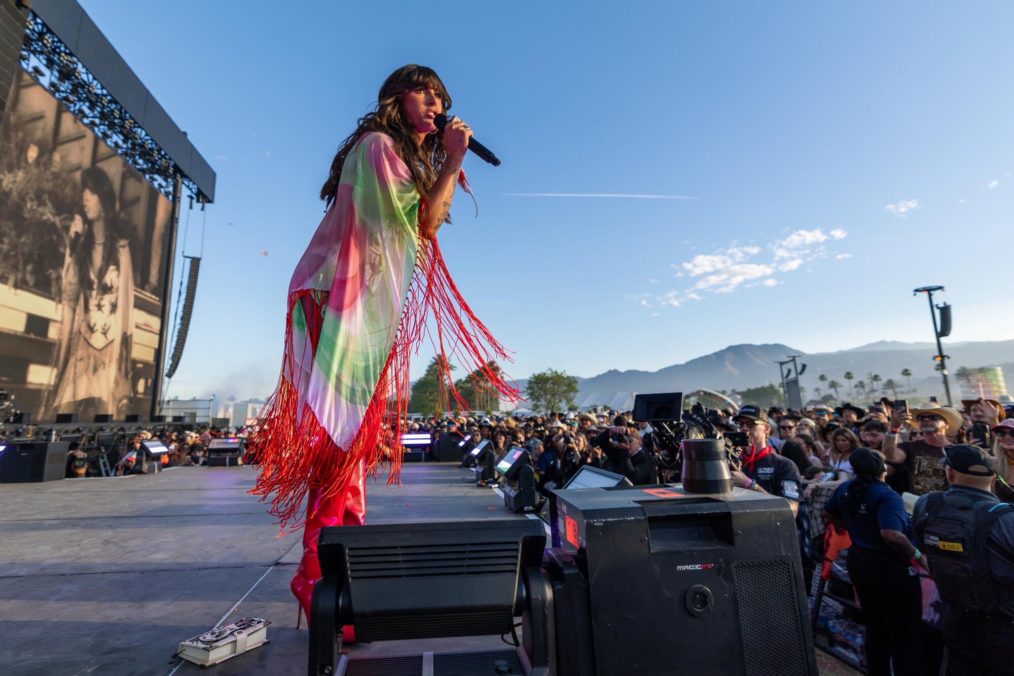 Ella Langley performs on alarge stage with blue sky and mountains behind her at Stagecoach