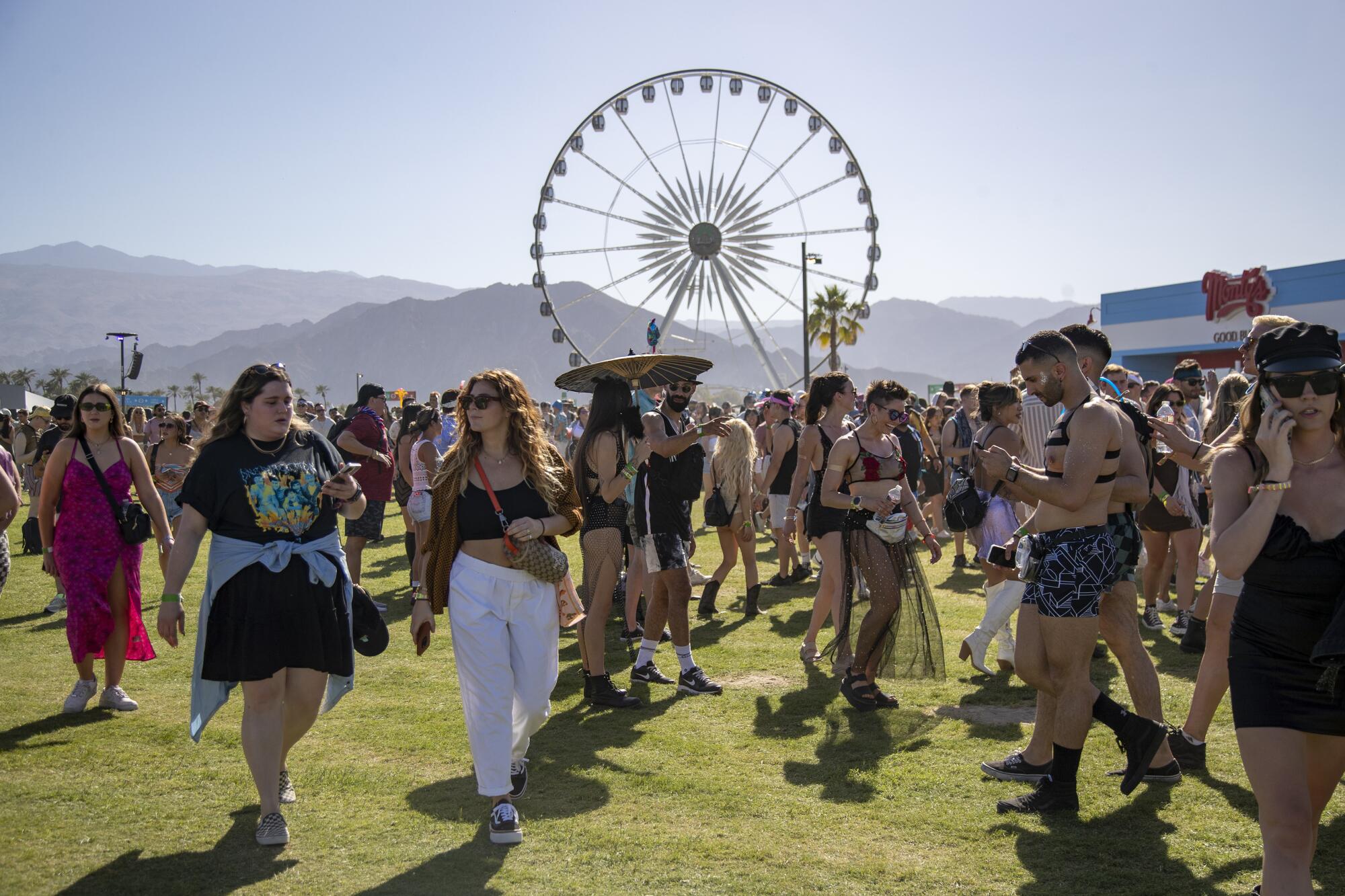  Crowds pour into the Coachella festival with a ferris wheel and mountains behind them